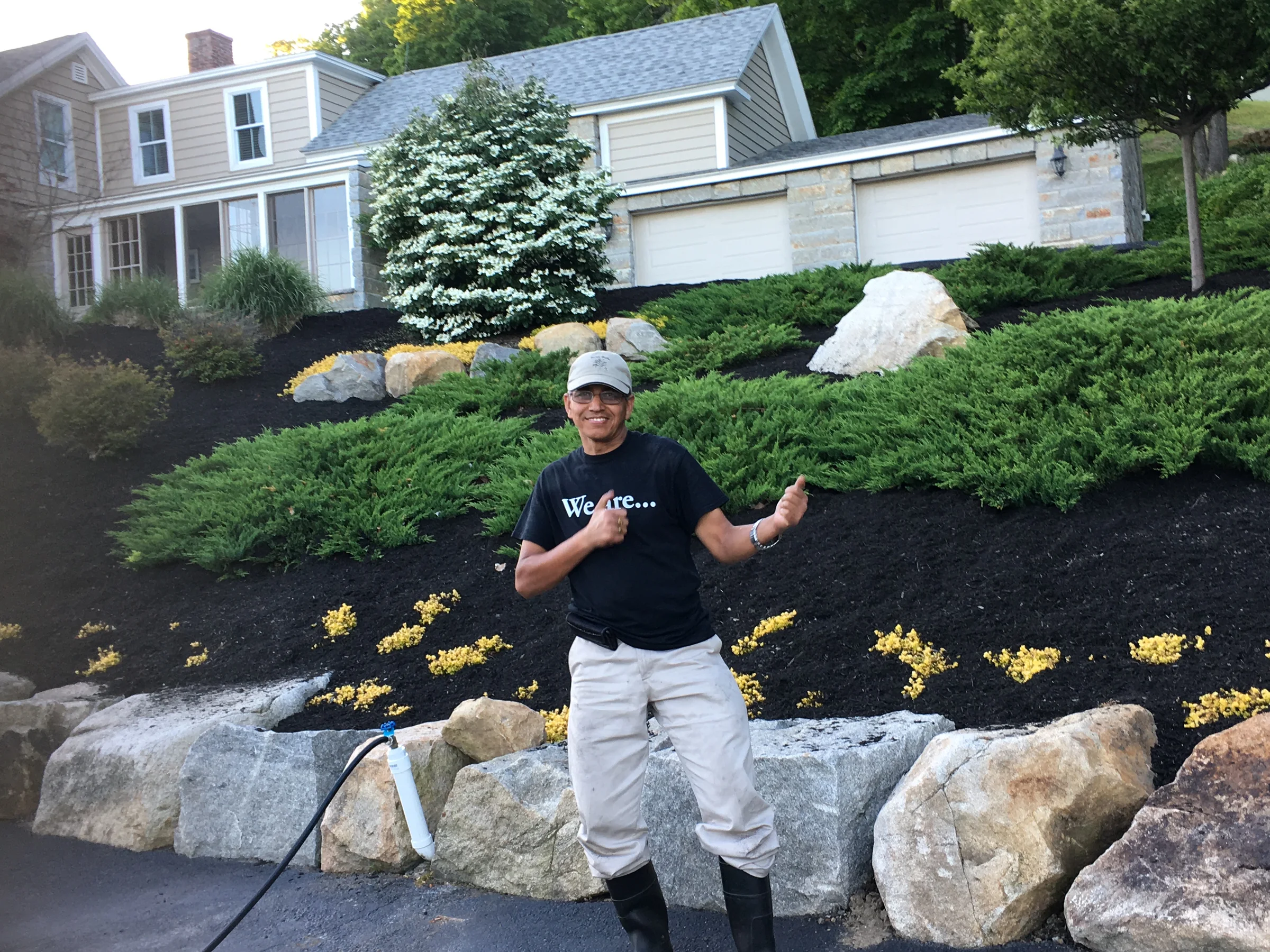 Worker standing in front of a finished residential rock garden with shrubs and fresh dark mulch