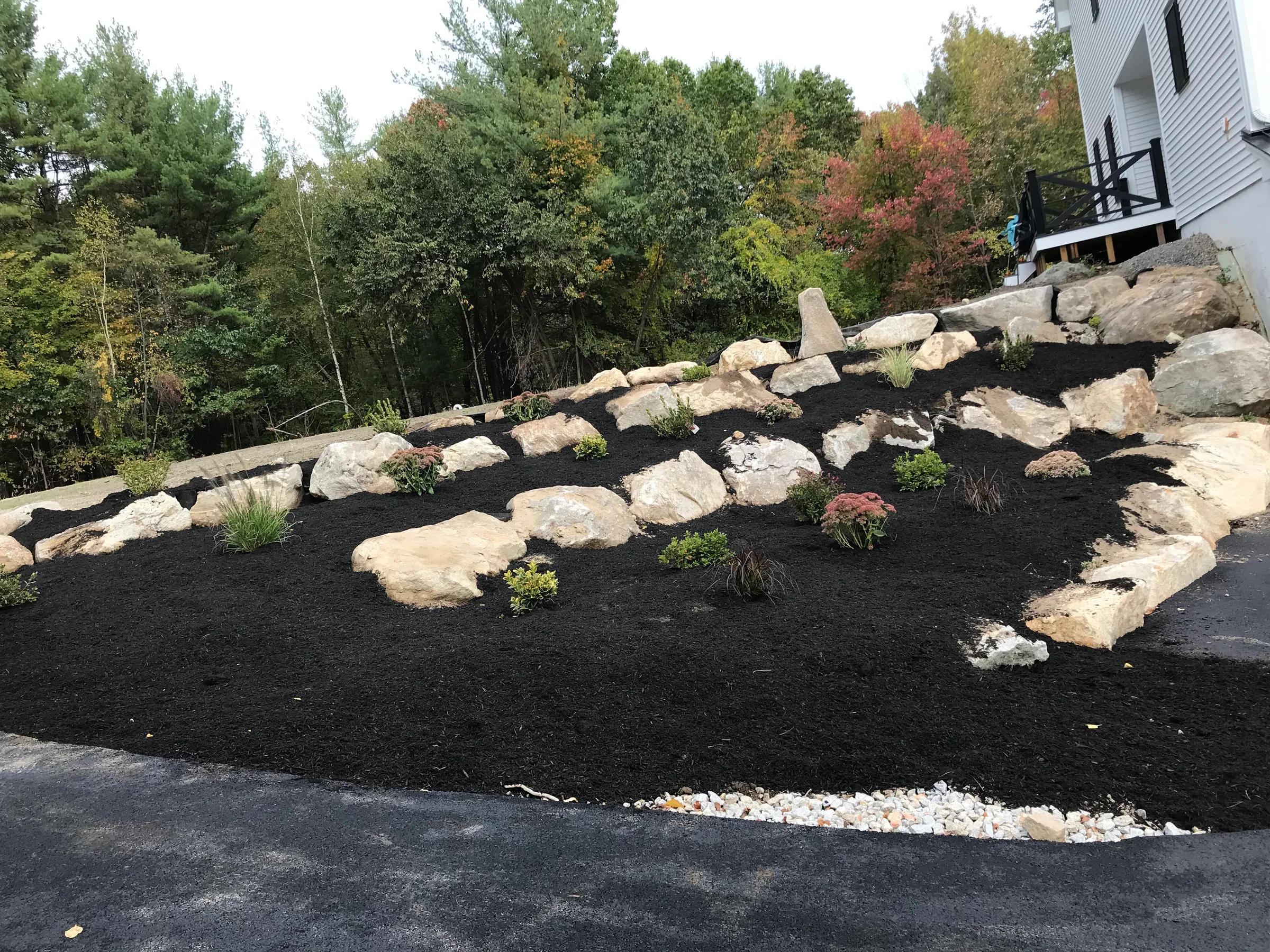 Finished sloped landscape with fresh dark mulch, boulders, and new plantings beside a home